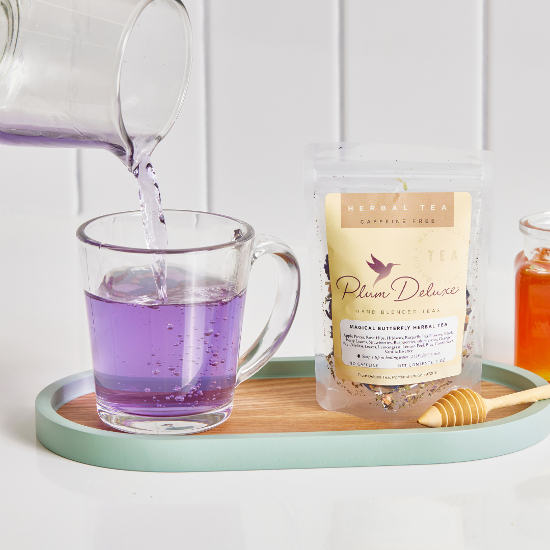 Plum Deluxe Magical Butterfly Herbal Tea featuring butterfly pea flower and berries, displayed in a clear glass cup.
