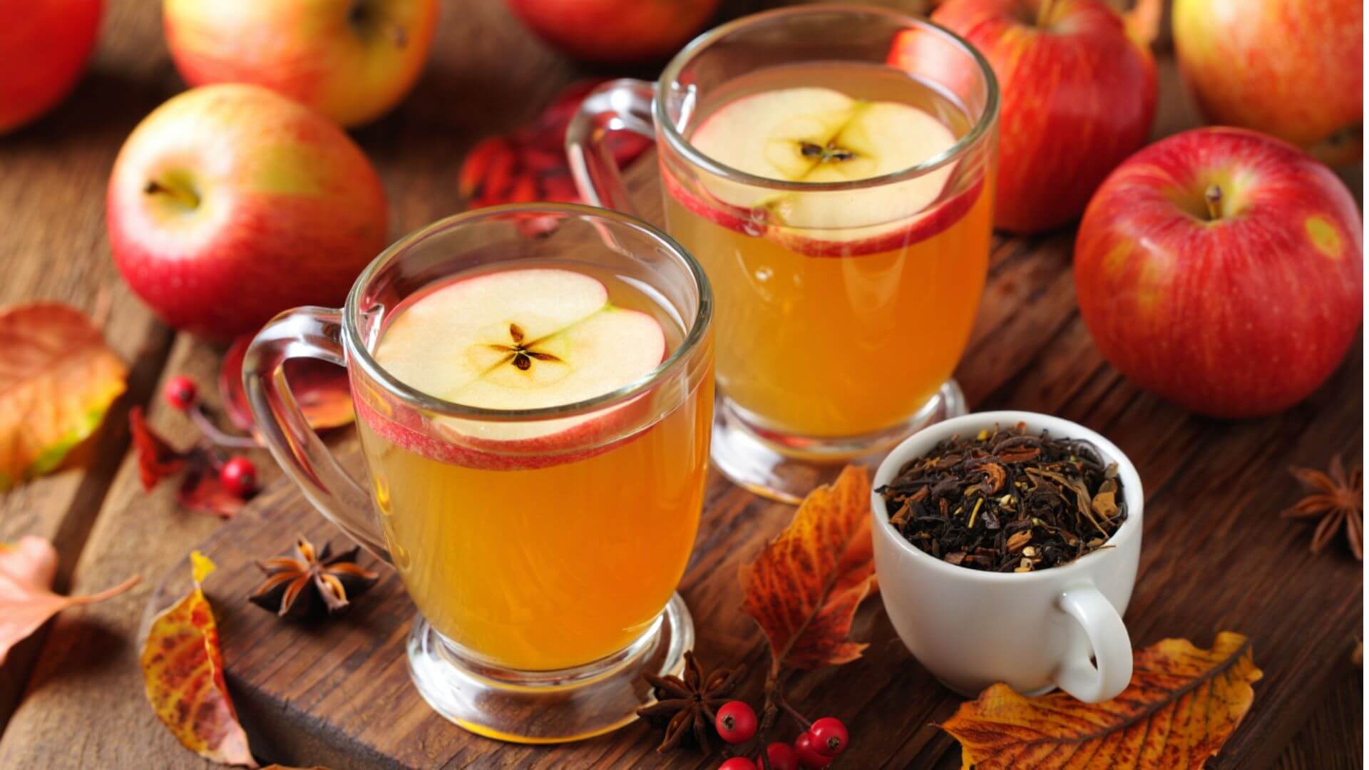 2 apple teas with loose leaf in a cup on the side, surrounded by apple fruits