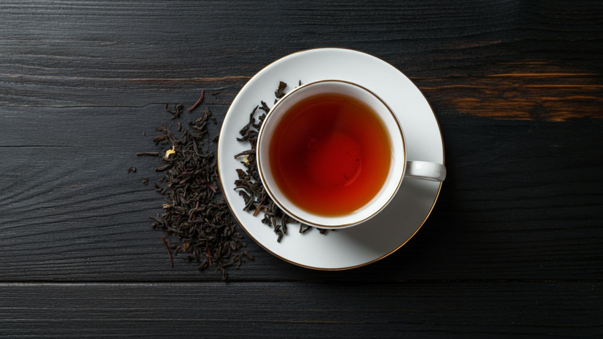 A white porcelain teacup filled with deep decaf black tea, resting on a matching saucer with loose leaf tea on the side