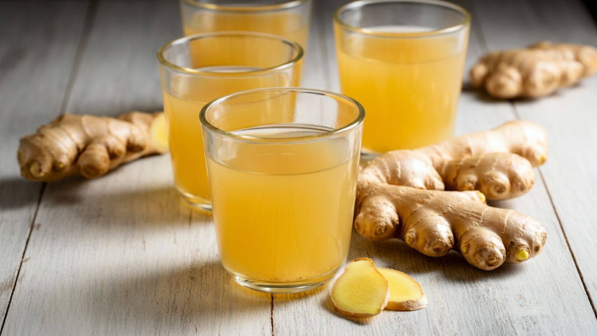 An organized glasses filled with ginger tea, while gingers are scattered on the table