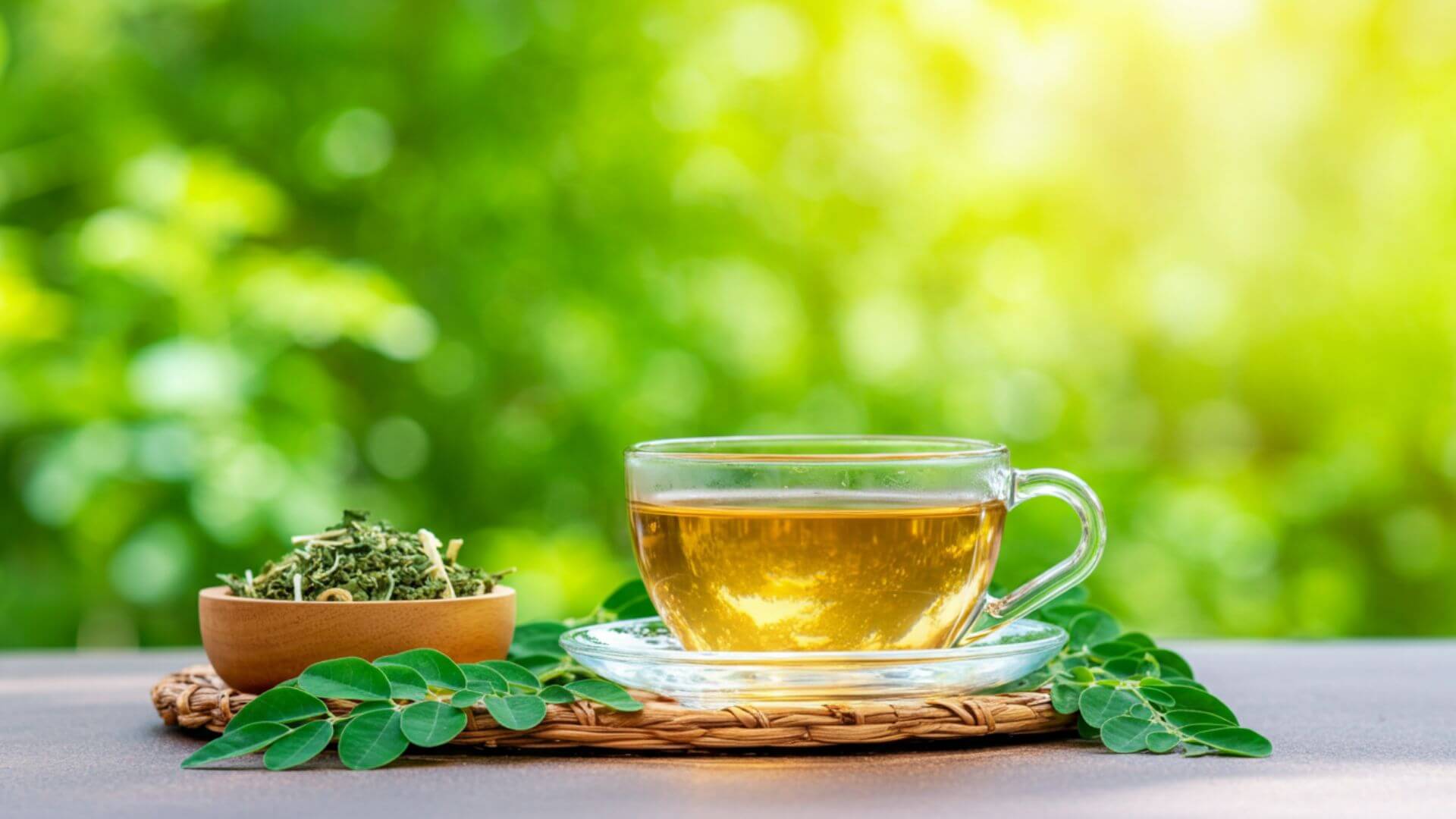 A clear glass teacup filled with warm golden moringa tea