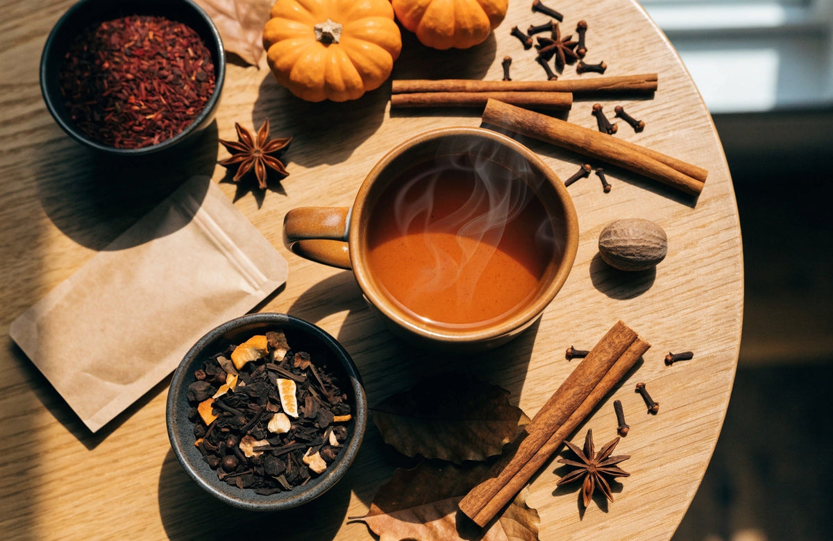 A mug of pumpkin spice tea with loose-leaf black tea, rooibos, cinnamon sticks, star anise, cloves and small pumpkins on an oak table