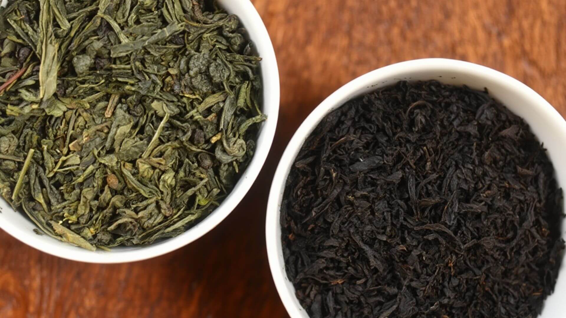 Green tea and black tea leaves in a bowl beside each other