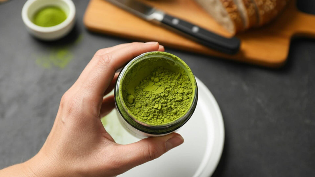 A hand holds an open jar of green matcha powder