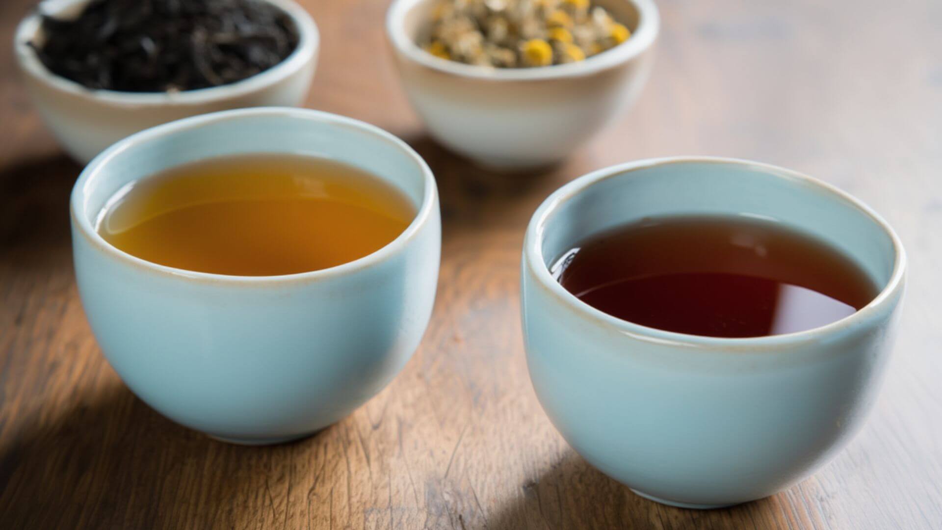 Herbal and black tea in a white teacup, and a chamomile and black loose leaf in a bowl