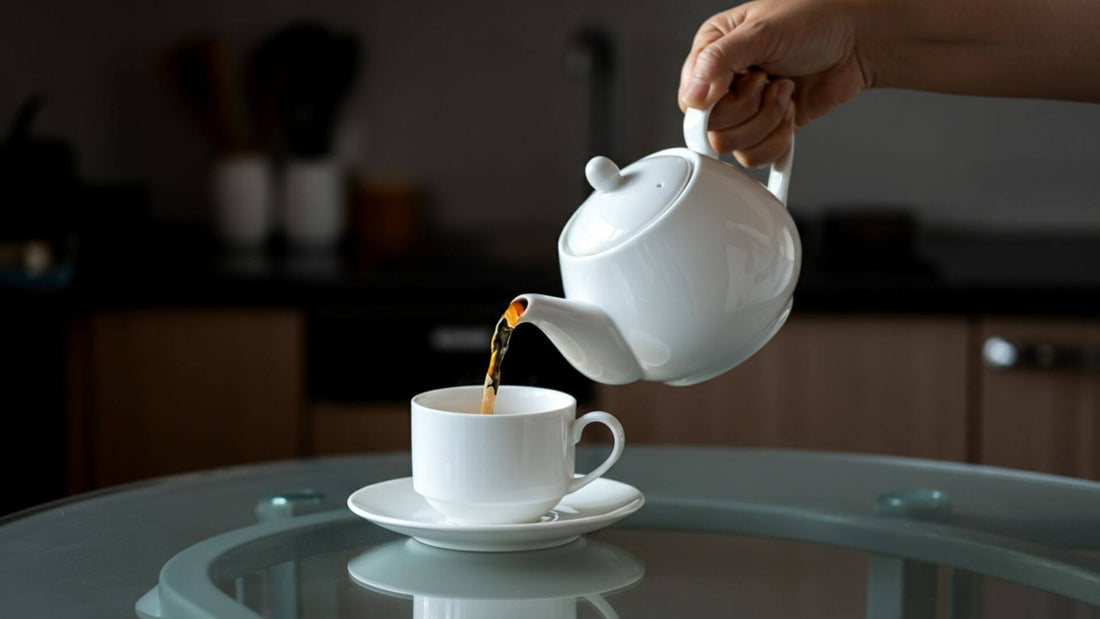 Hand pouring tea from a white teapot into a matching teacup