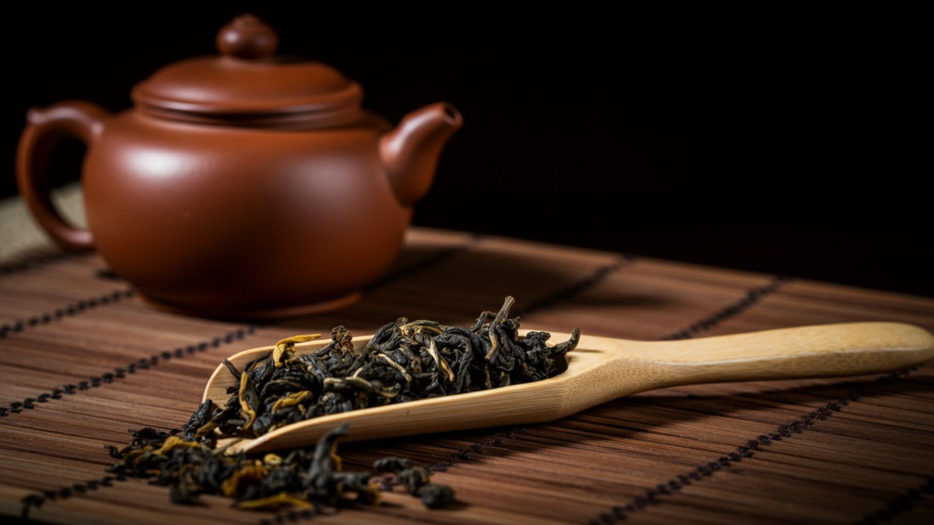 A scoop of Oolong tea leaves with a teapot in the background