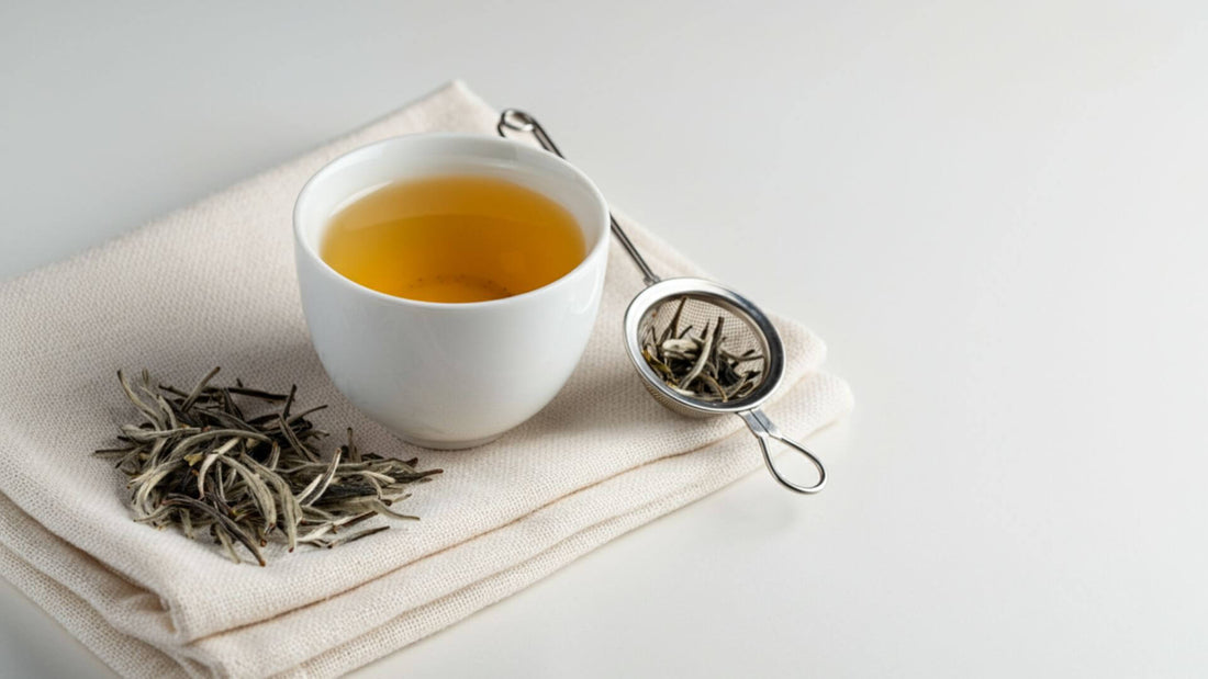 White tea in a cup with dried white tea leaves and strainer beside