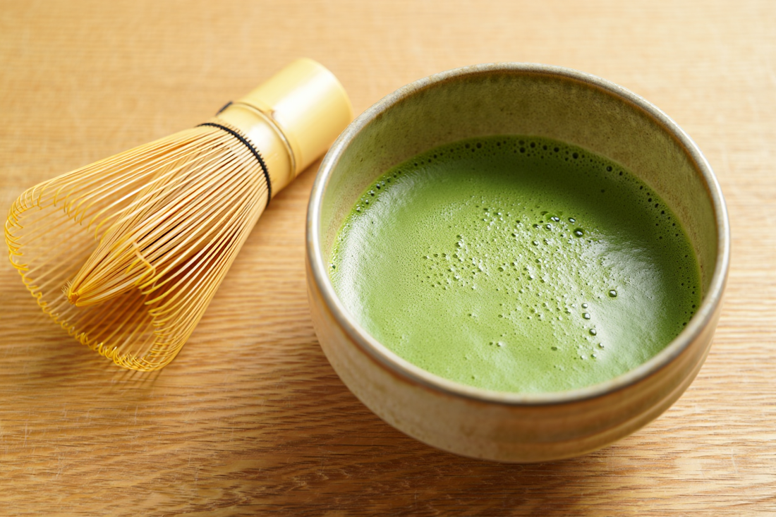 A bowl of freshly whisked bright green matcha with fine foam and a bamboo whisk