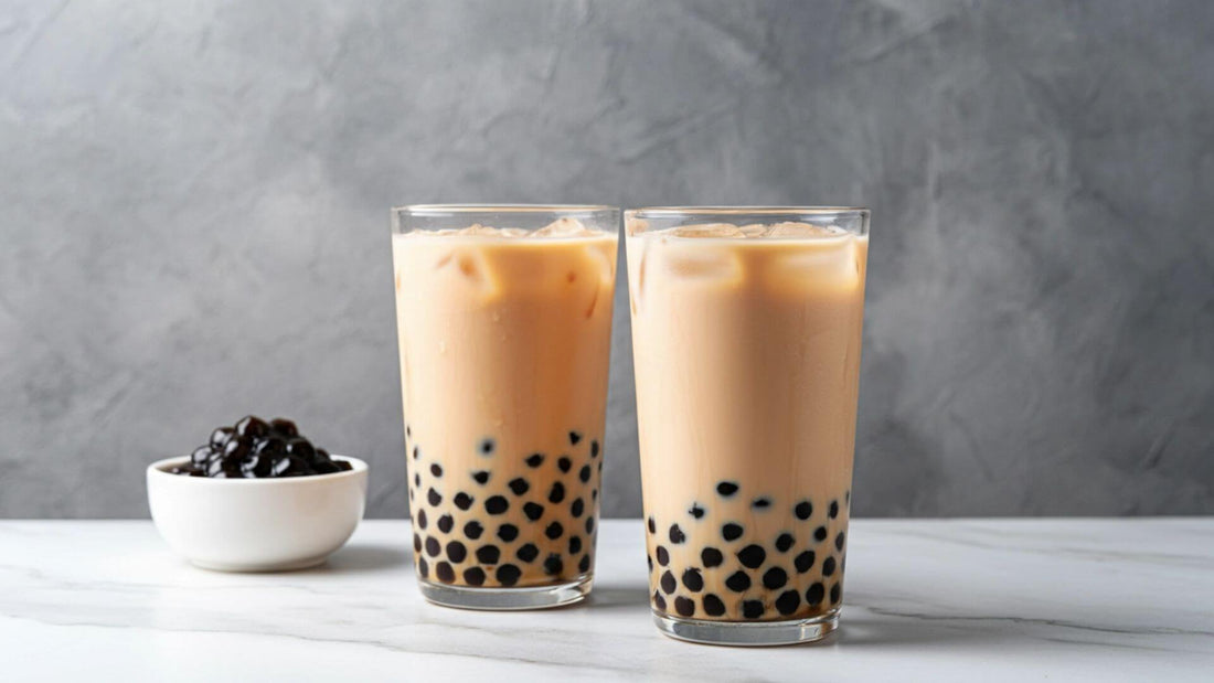 Two glasses of milk tea with tapioca pearls in a bowl on the side
