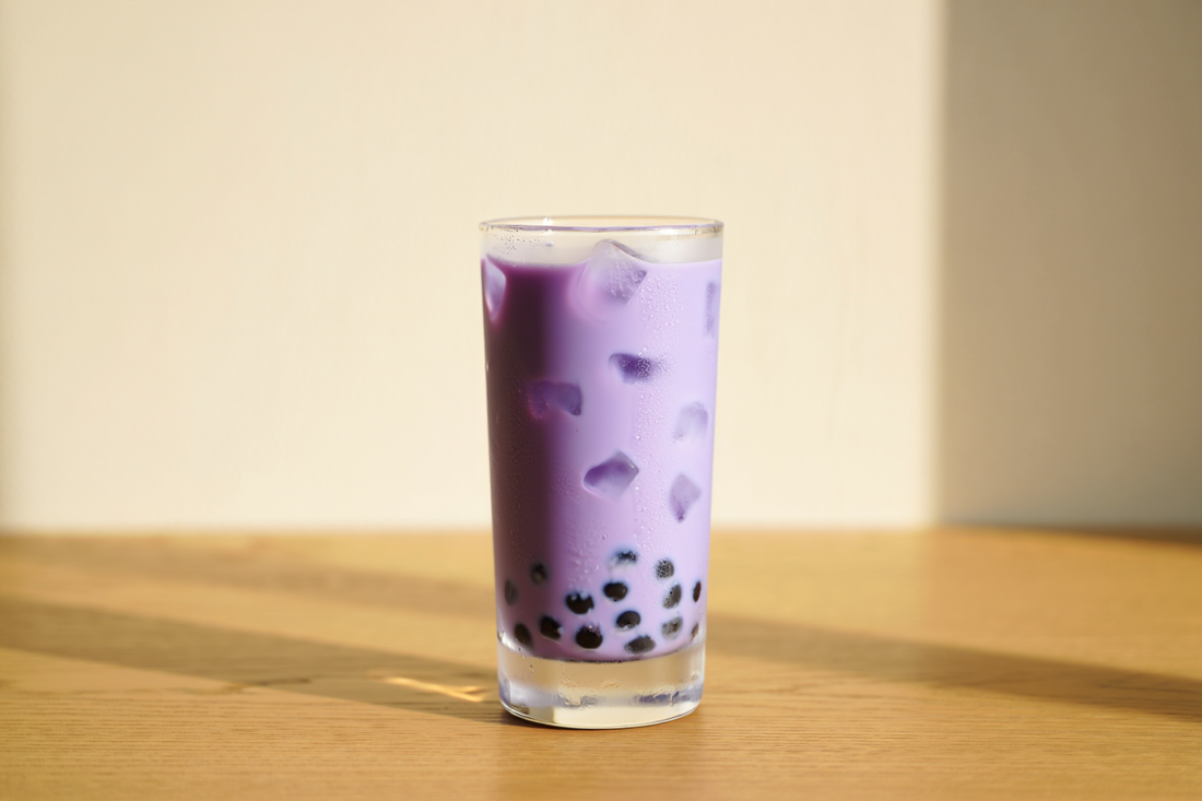 Tall glass of iced purple ube milk tea with black boba pearls on an oak table