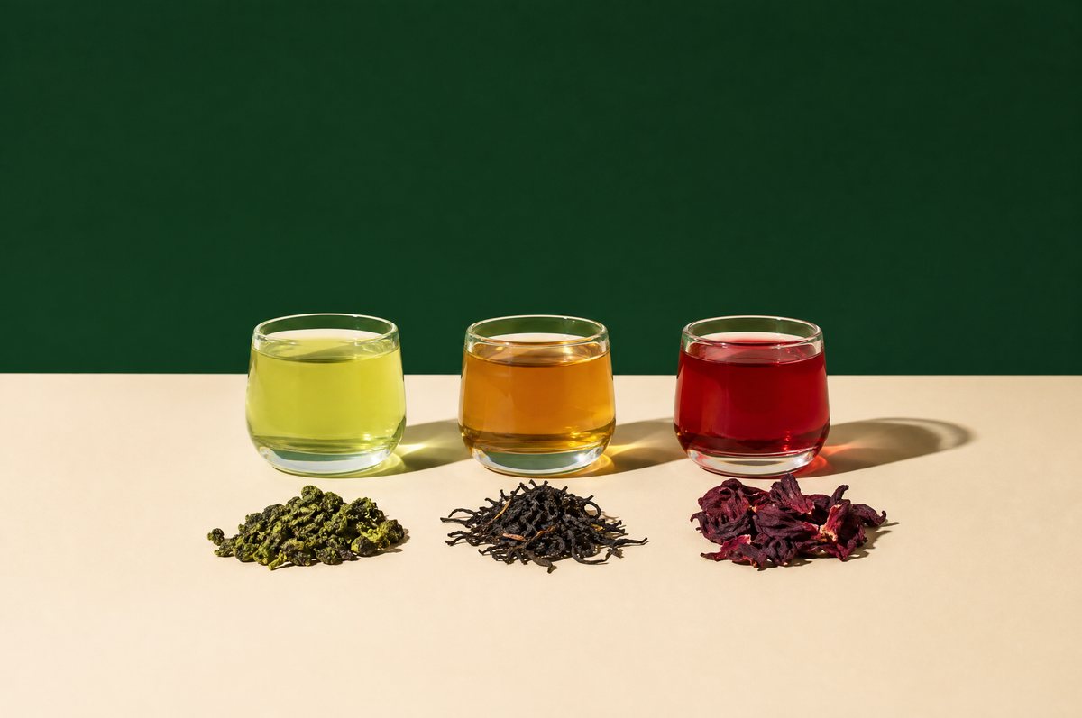Three small clear glass cups in a row filled with teas of different colors, pale green, golden amber and ruby red