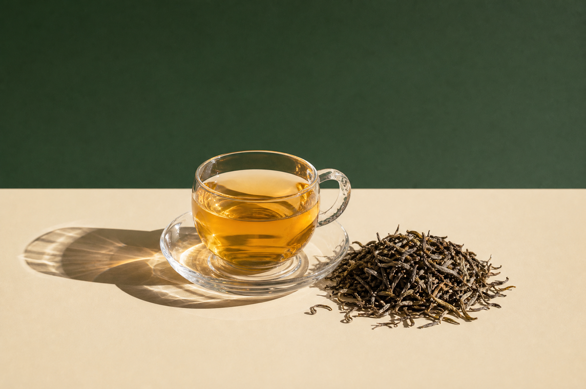 A delicate clear glass teacup on a clear glass saucer filled with bright pale golden-amber Darjeeling tea