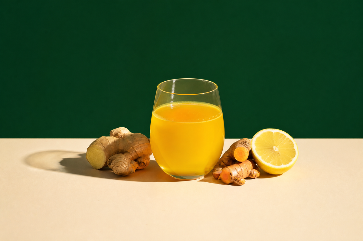 A stemless clear glass cup of bright golden turmeric-ginger herbal tea, beside a knob of fresh ginger root