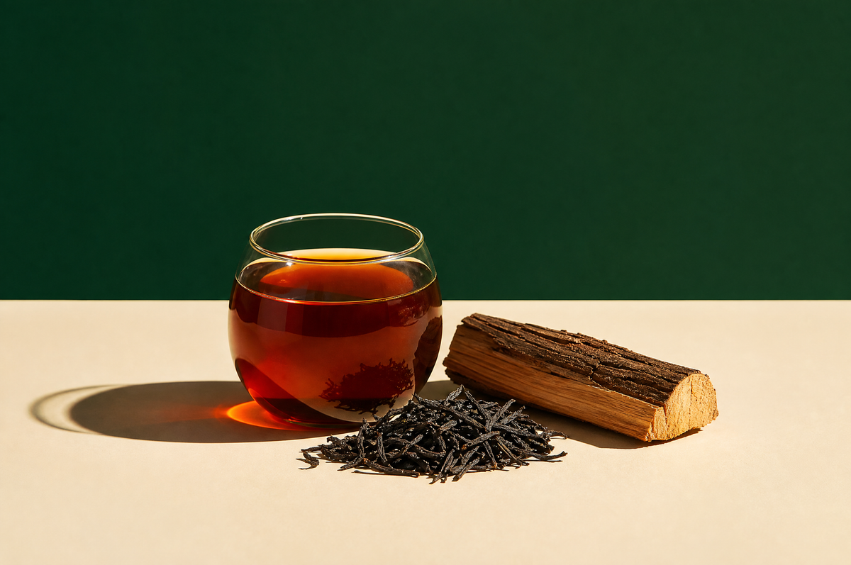 A round clear glass cup of deep amber-red smoky black tea, beside a small heap of long, twisted