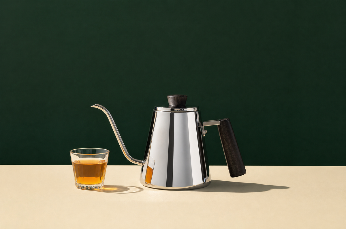A polished stainless steel stovetop gooseneck kettle with a long slender curved spout and a black wooden handle