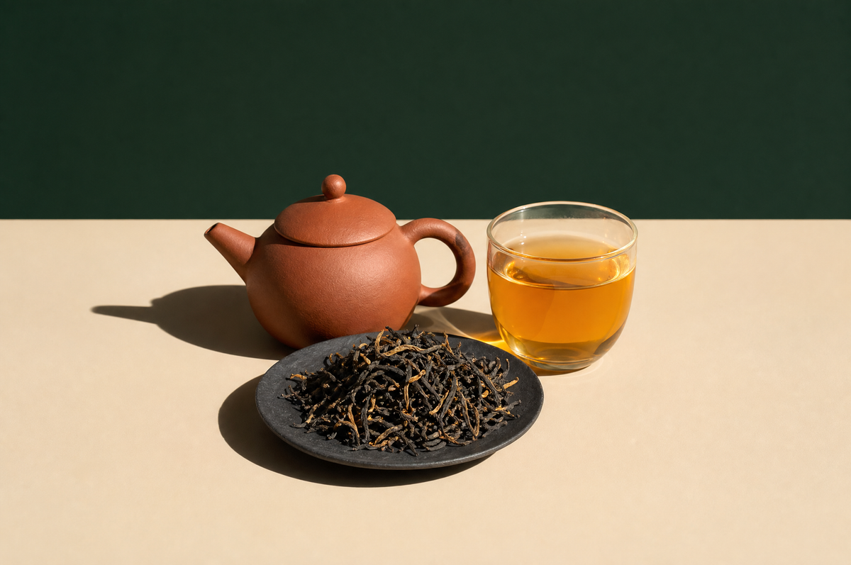 A small unglazed reddish-brown clay teapot beside a clear glass cup of bright amber-gold black tea
