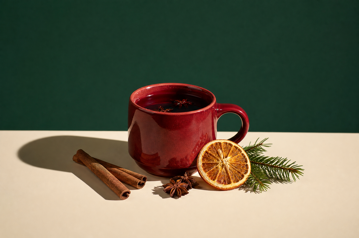 A dark red glazed ceramic mug of ruby-red hibiscus spiced tea, with a few whole star anise, two cinnamon sticks