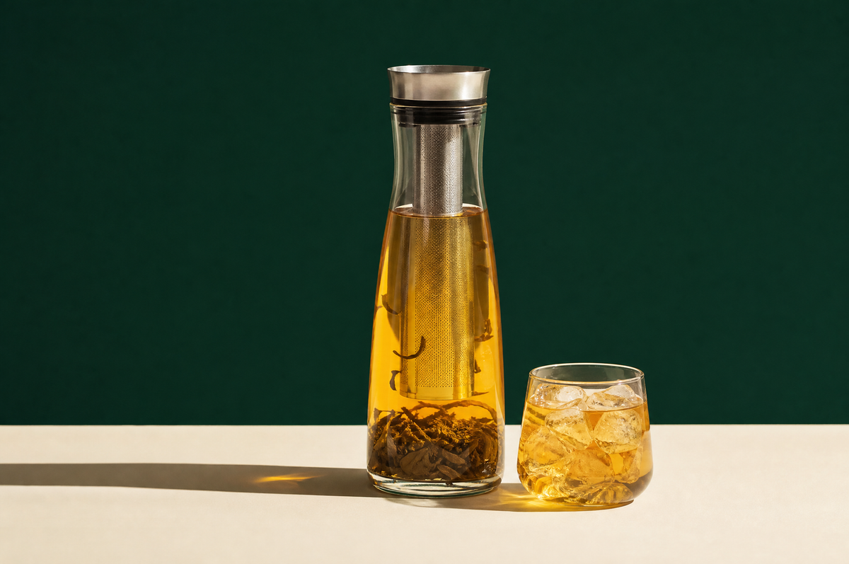 A tall slim clear glass cold-brew tea carafe with a narrow stainless steel mesh filter inside