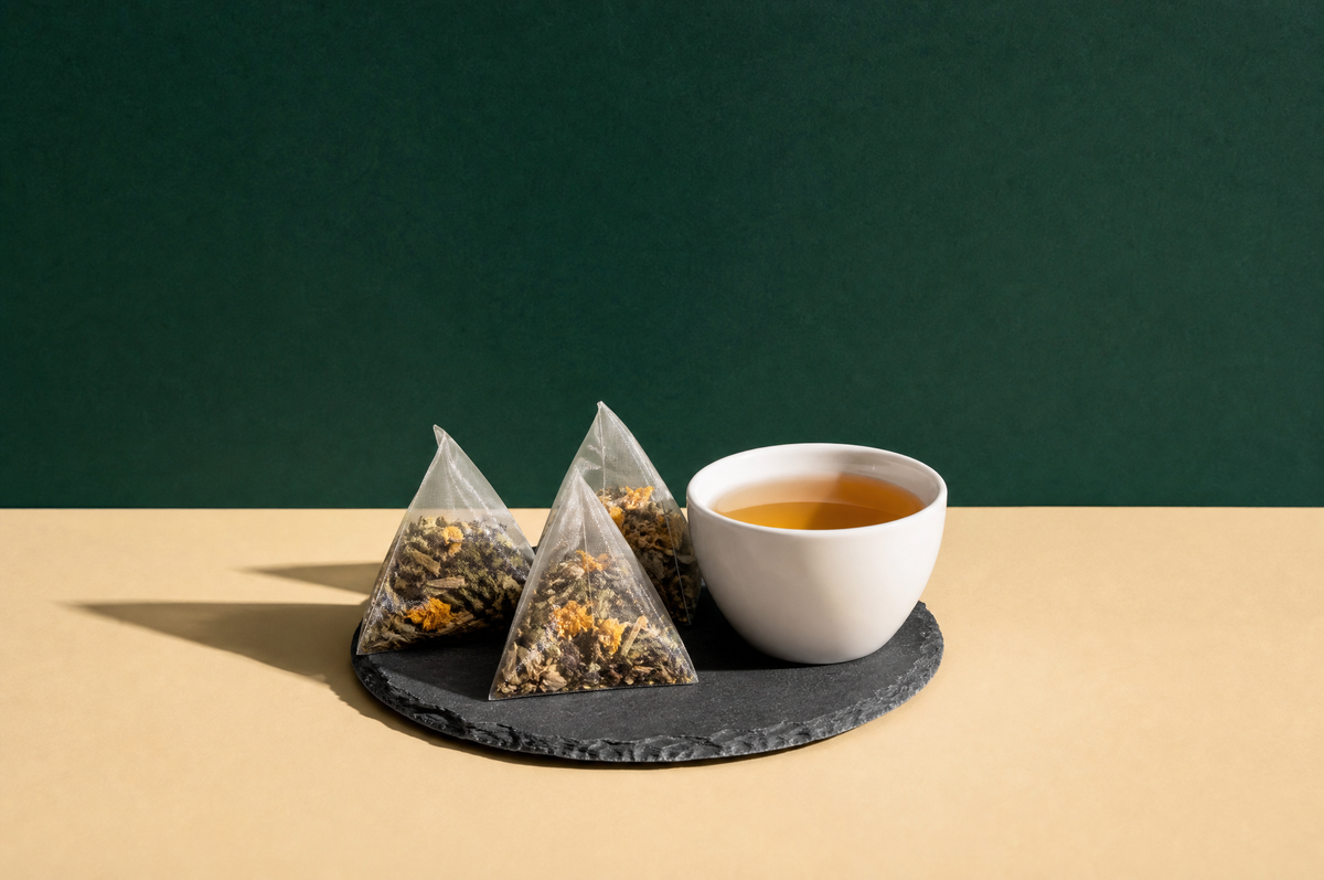 Three translucent pyramid-shaped mesh tea sachets filled with visible whole-leaf tea and dried herbs