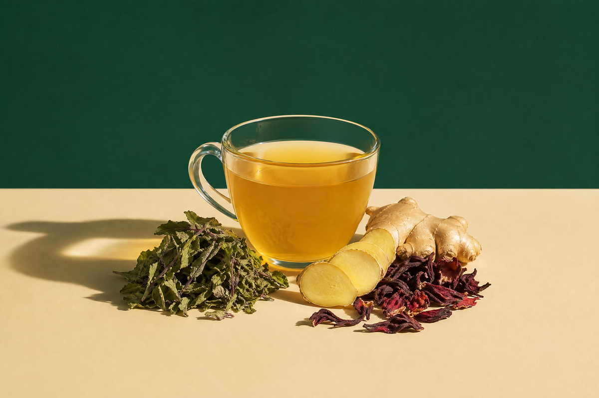 A clear glass cup of golden-yellow turmeric ginger herbal tea beside a small loose pile of dried tulsi leaves