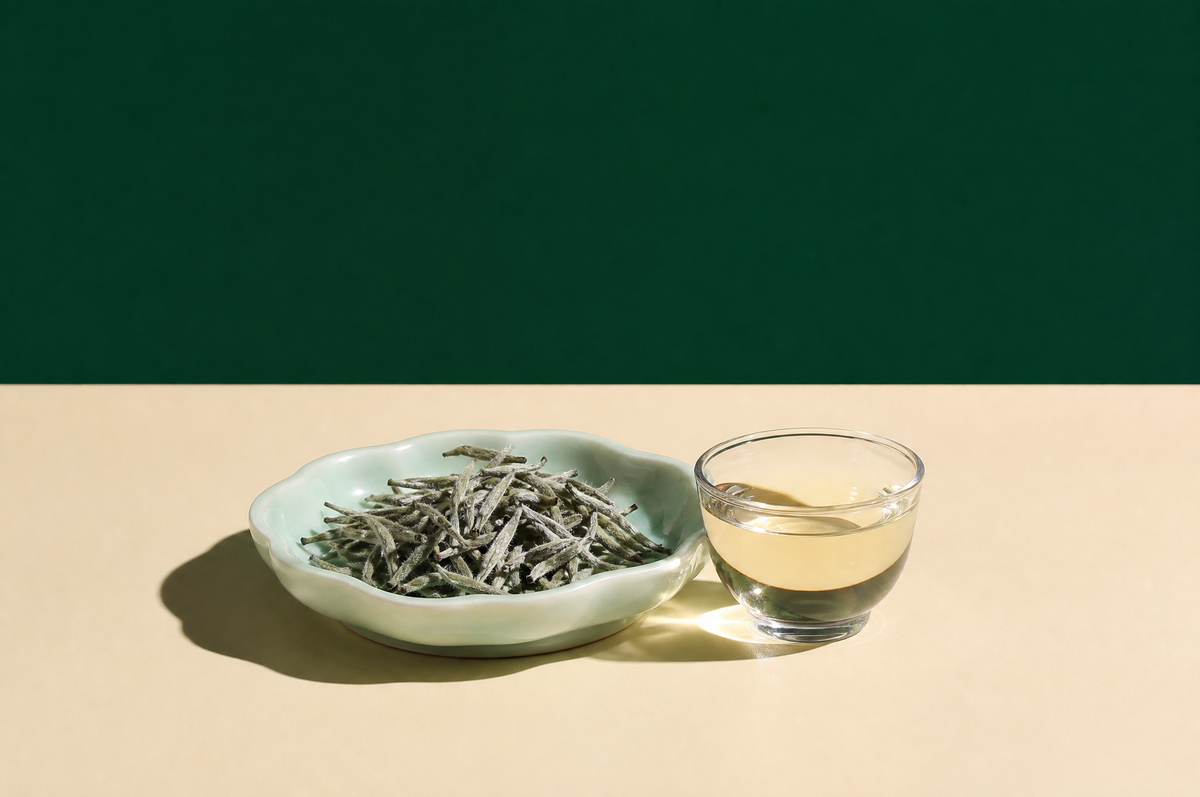 A shallow pale celadon ceramic dish holding a small heap of silvery, downy silver-needle white tea buds