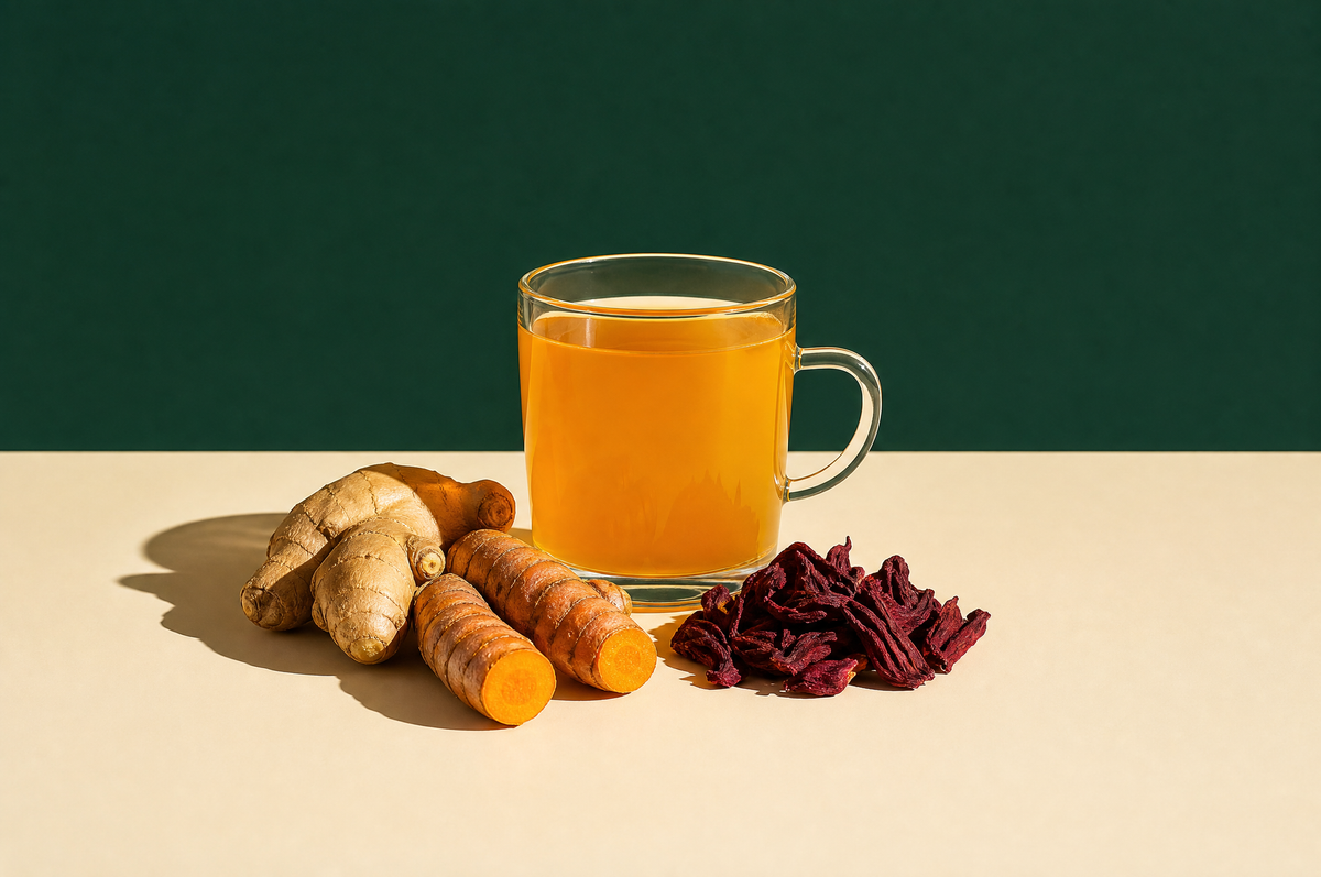 A clear glass mug of golden-orange turmeric ginger herbal tea, beside a knob of fresh ginger root
