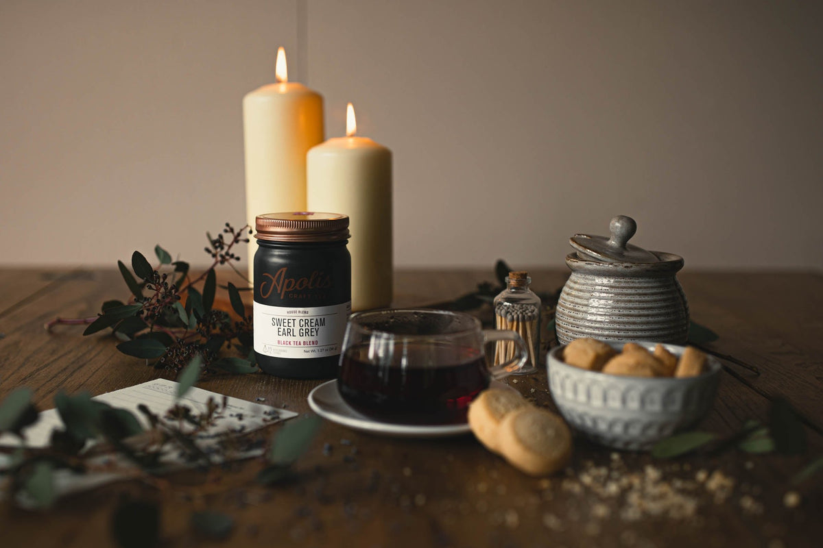 Apolis Craft Tea jar of Sweet Cream Earl Grey beside a glass cup of tea, cookies and candles
