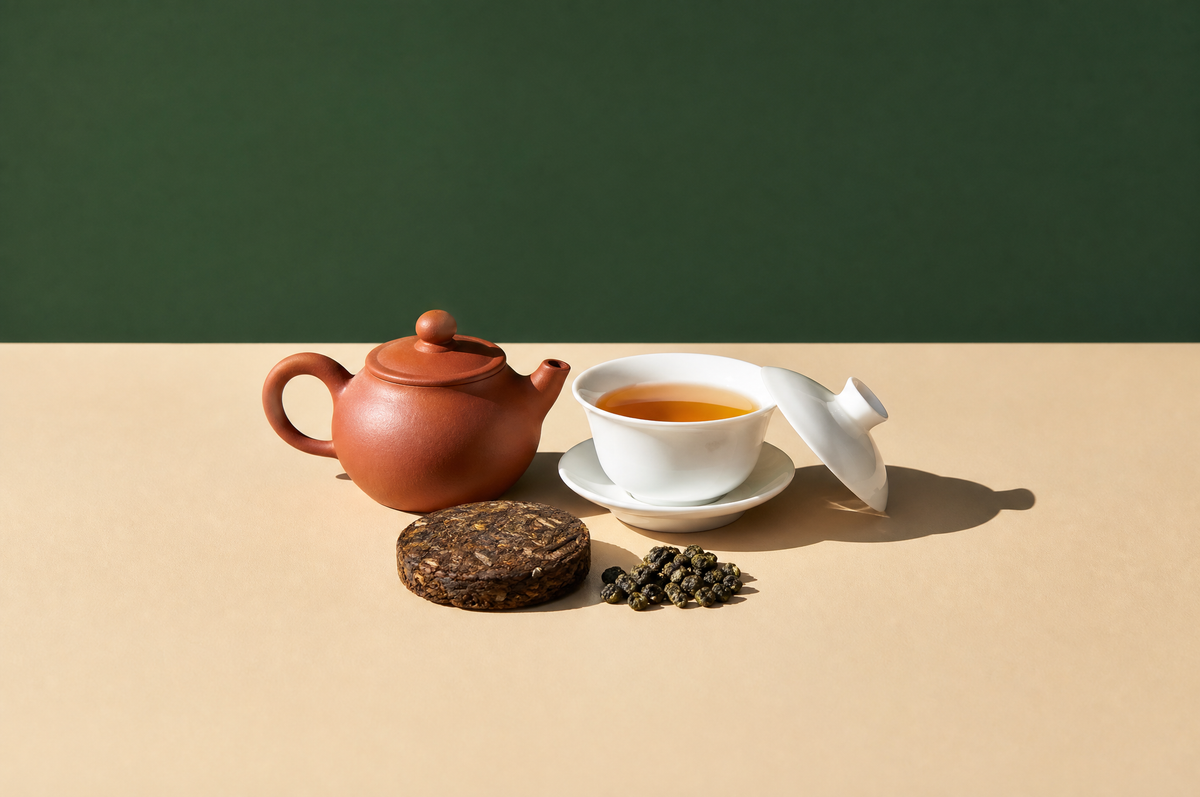 A small unglazed reddish-brown clay teapot, a white porcelain gaiwan with lid holding golden-amber oolong tea