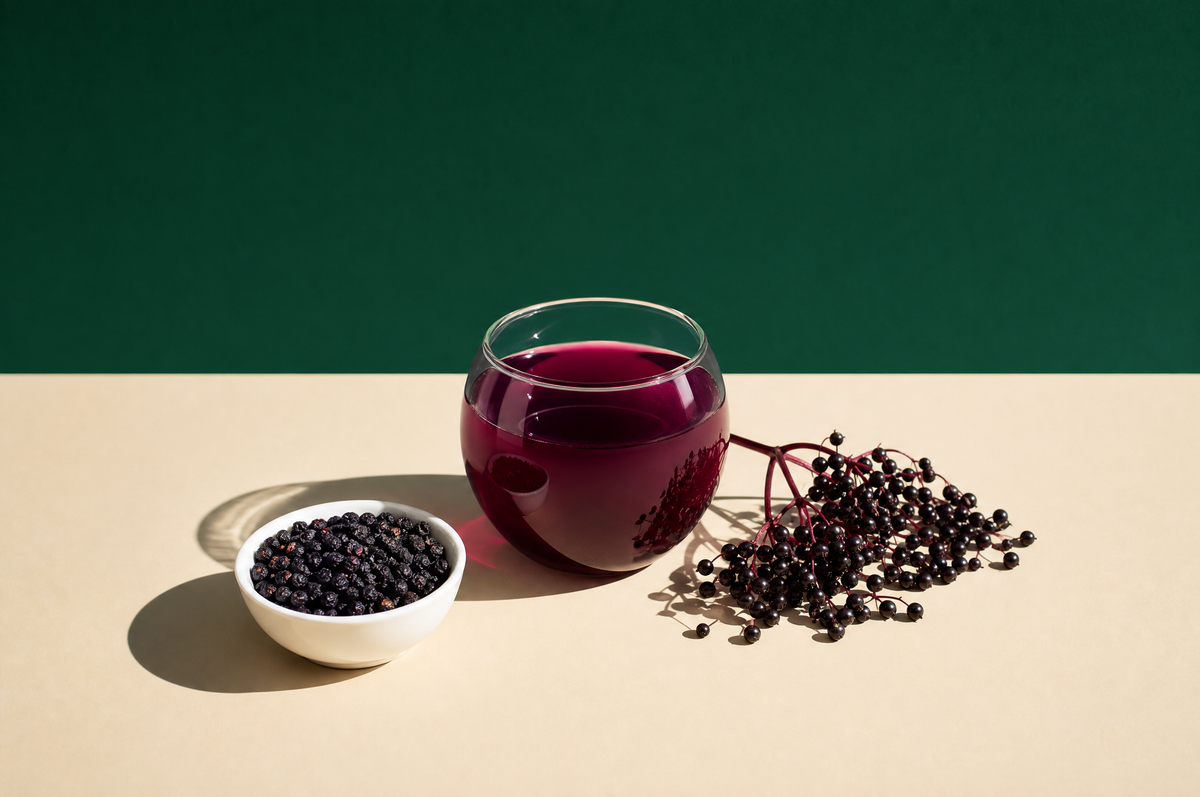 A round clear glass cup of deep purple-red elderberry tea, a small white ceramic bowl of dried dark elderberries
