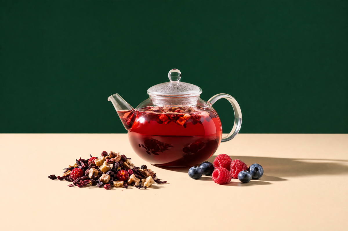 A round clear glass teapot of ruby-red fruit infusion, a small heap of dried fruit tea mix with dried apple pieces