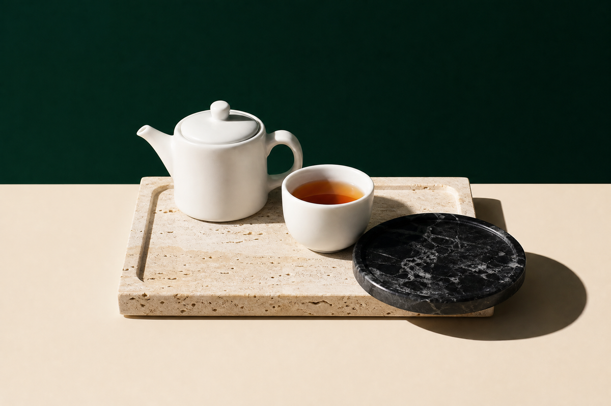 A rectangular cream travertine marble serving tray with a small round black marble tray overlapping its corner; on the