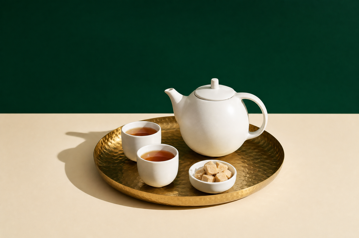 A round hammered-brass serving tray holding a plain white ceramic teapot