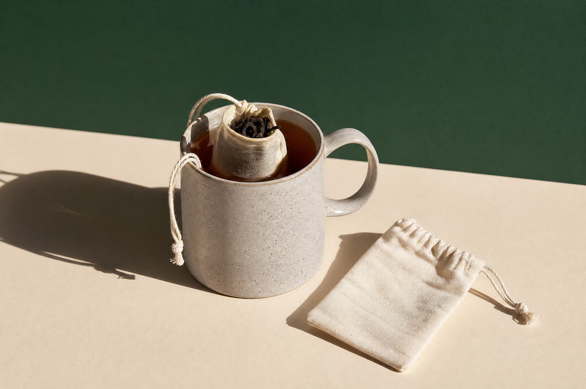 Two plain unbleached cotton muslin reusable tea bags with drawstrings: one filled with twisted dark loose black tea leaves