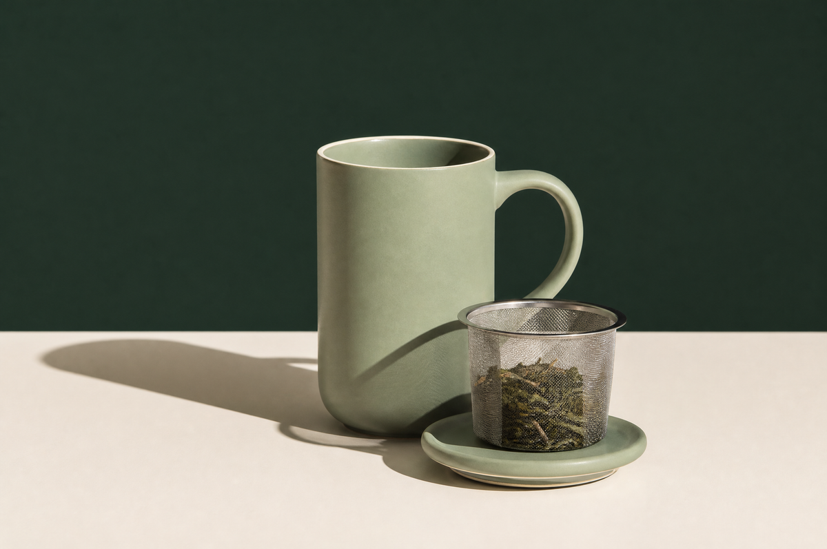 A tall matte sage-green ceramic tea mug with a handle and a matching ceramic lid set beside it