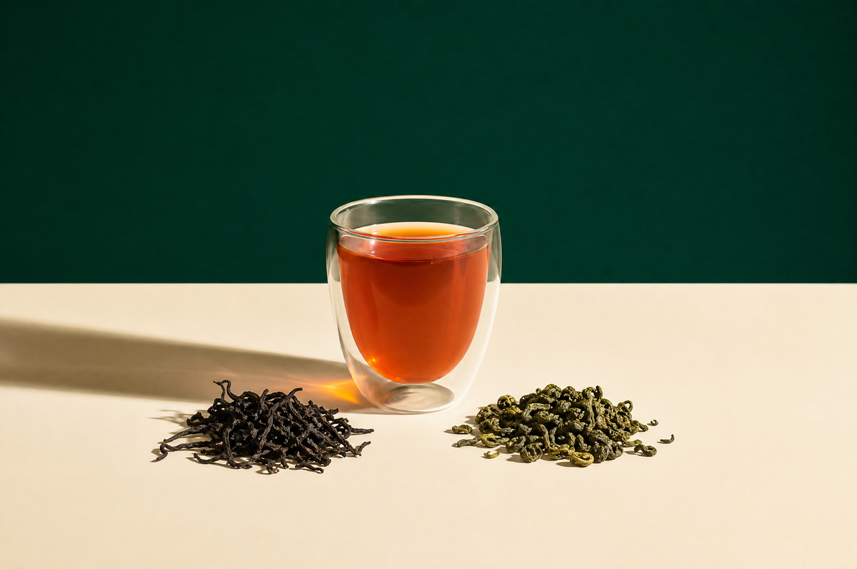 A clear double-walled glass cup of bright amber-copper black tea beside two small separate heaps of loose tea: twisted dark