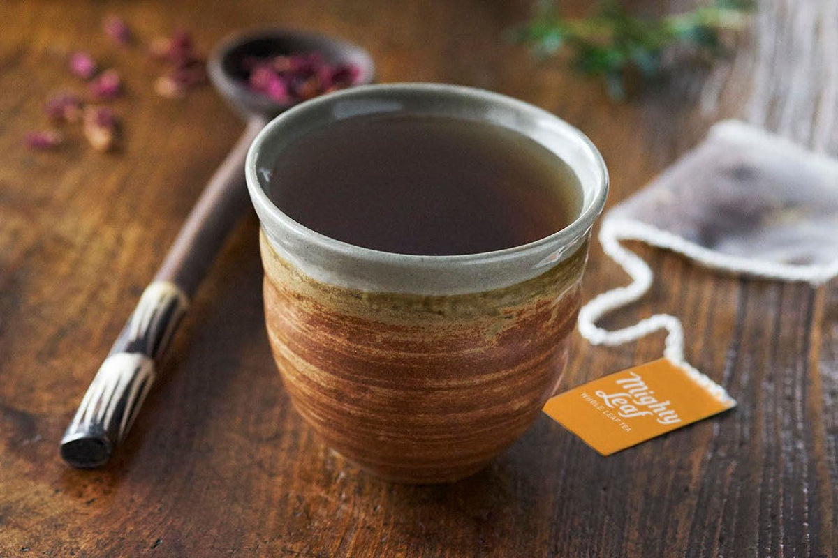 Mighty Leaf whole leaf tea pouch beside a ceramic cup of tea on a wooden table