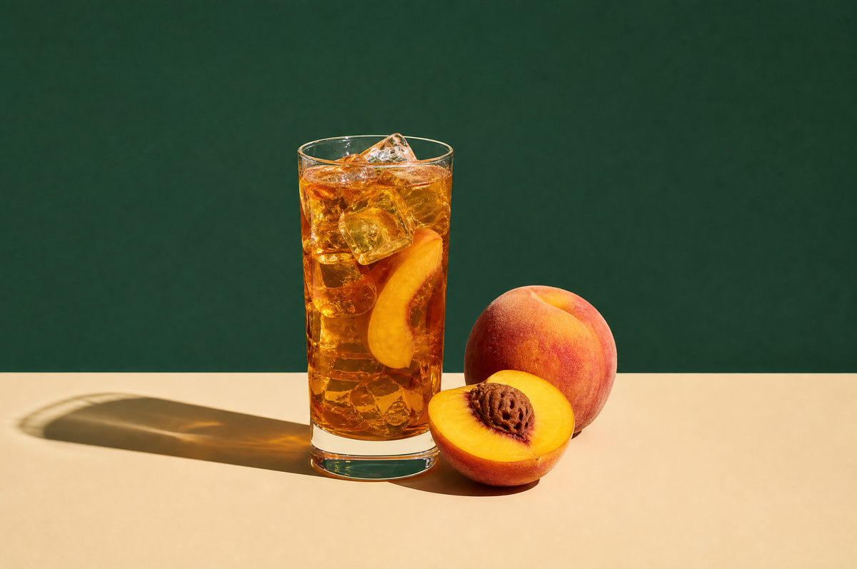 A tall clear glass of iced amber peach black tea with clear ice cubes and a thin peach slice
