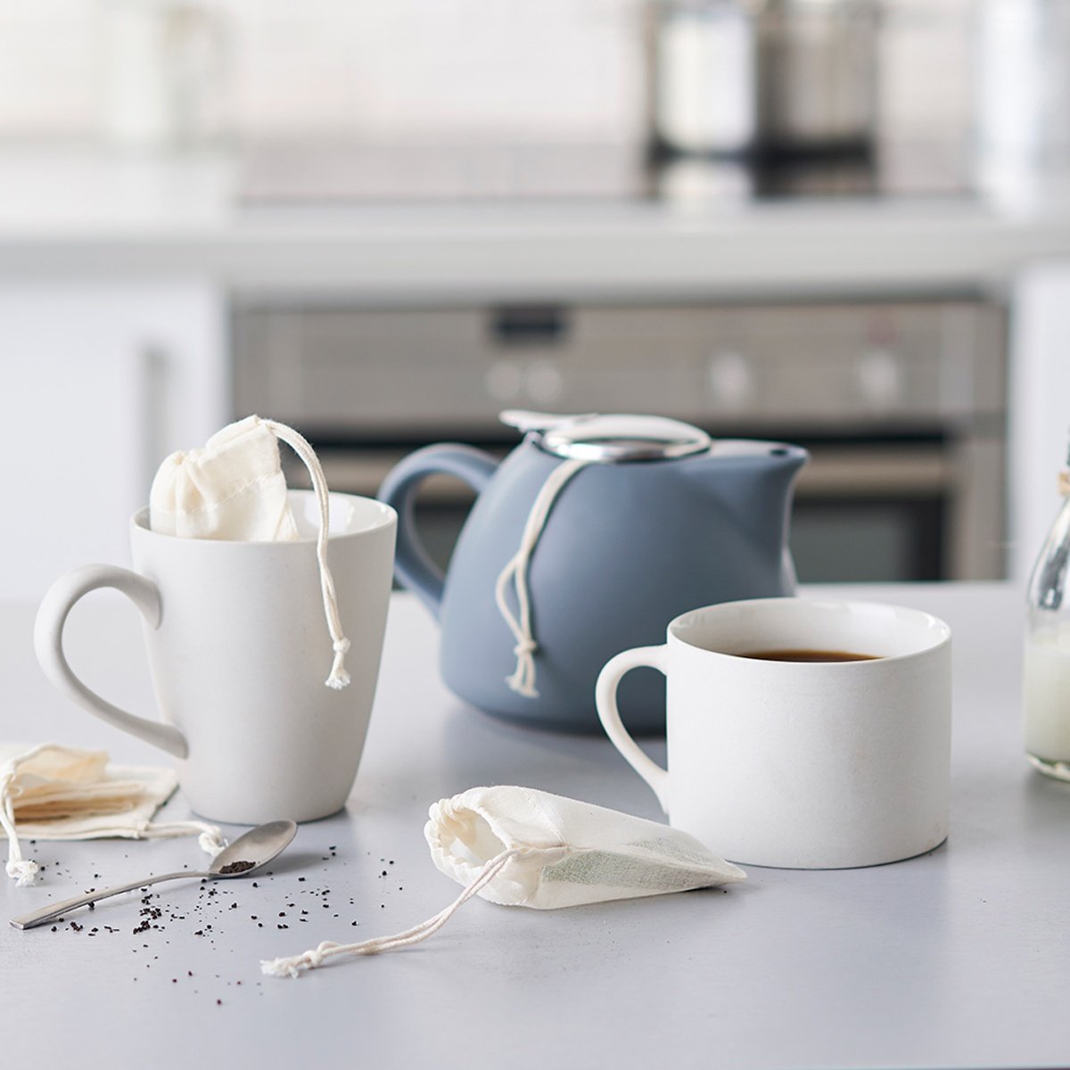 Reusable tea bags in a ceramic cup with a blue tea pot