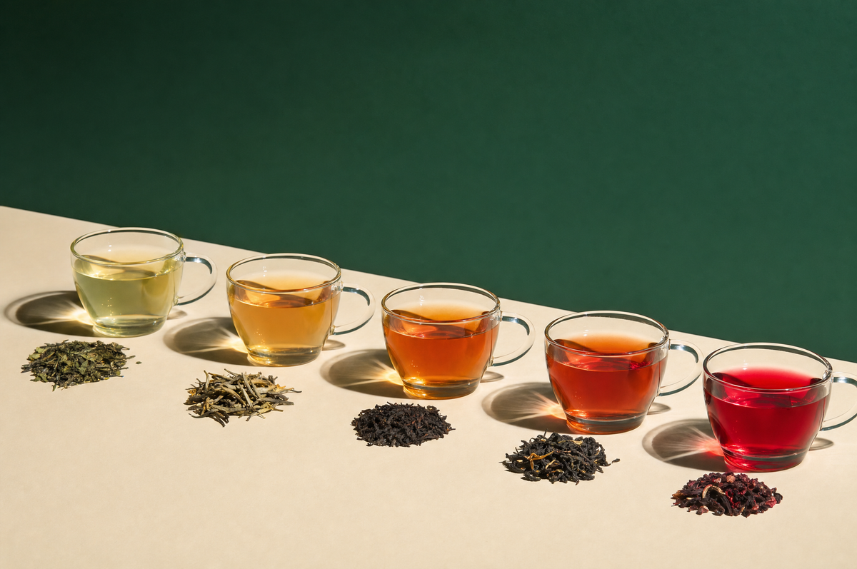 Glass cups of green, white, oolong, black and hibiscus tea with their dry leaves