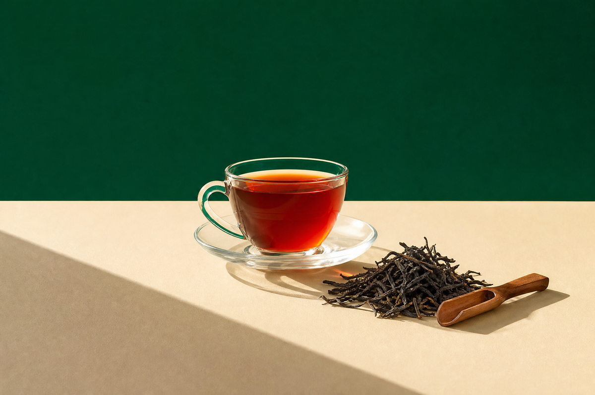 A clear glass teacup on a clear glass saucer filled with deep amber-red black tea
