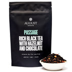 August Passage - Hazelnut Chocolate Black Tea in a cup with a tea bag, showcasing the product's packaging and rich color.
