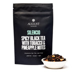 August Silencio - Spicy Pineapple Black Tea packaging displayed in a cup, featuring a vibrant design and clear branding.