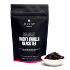 August Breakfast - Smoky Vanilla Black Tea in a bag, displayed in a cup with a teapot in the background.