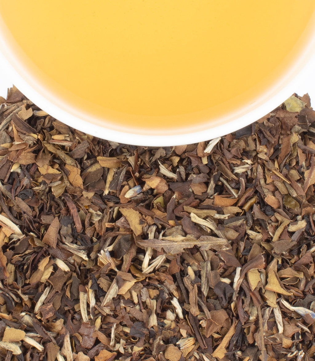 Close-up of dried tea leaves with a cup of tea in the background