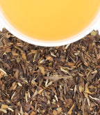 Close-up of dried tea leaves with a cup of tea in the background