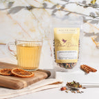 Plum Deluxe Bookshop Blend White Tea (Cinnamon / Black Currant) in a cup with a book in the background.