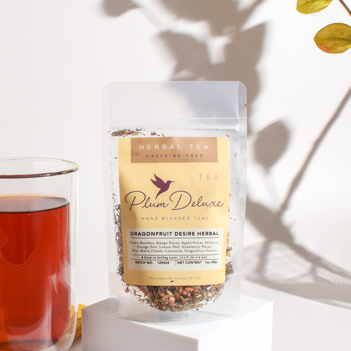 Plum Deluxe Dragonfruit Desire Herbal Tea in a cup, with vibrant dragonfruit and herbal ingredients visible in the background.