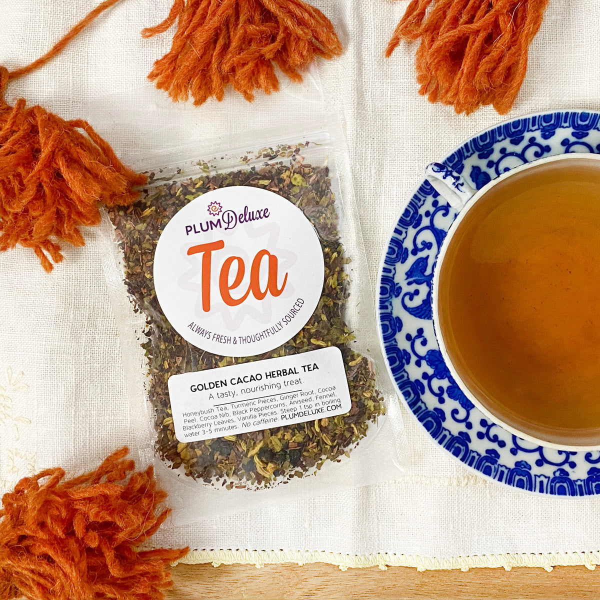 Plum Deluxe Golden Cacao Herbal Tea (Turmeric - Chocolate) in a square packaging on a wooden surface.