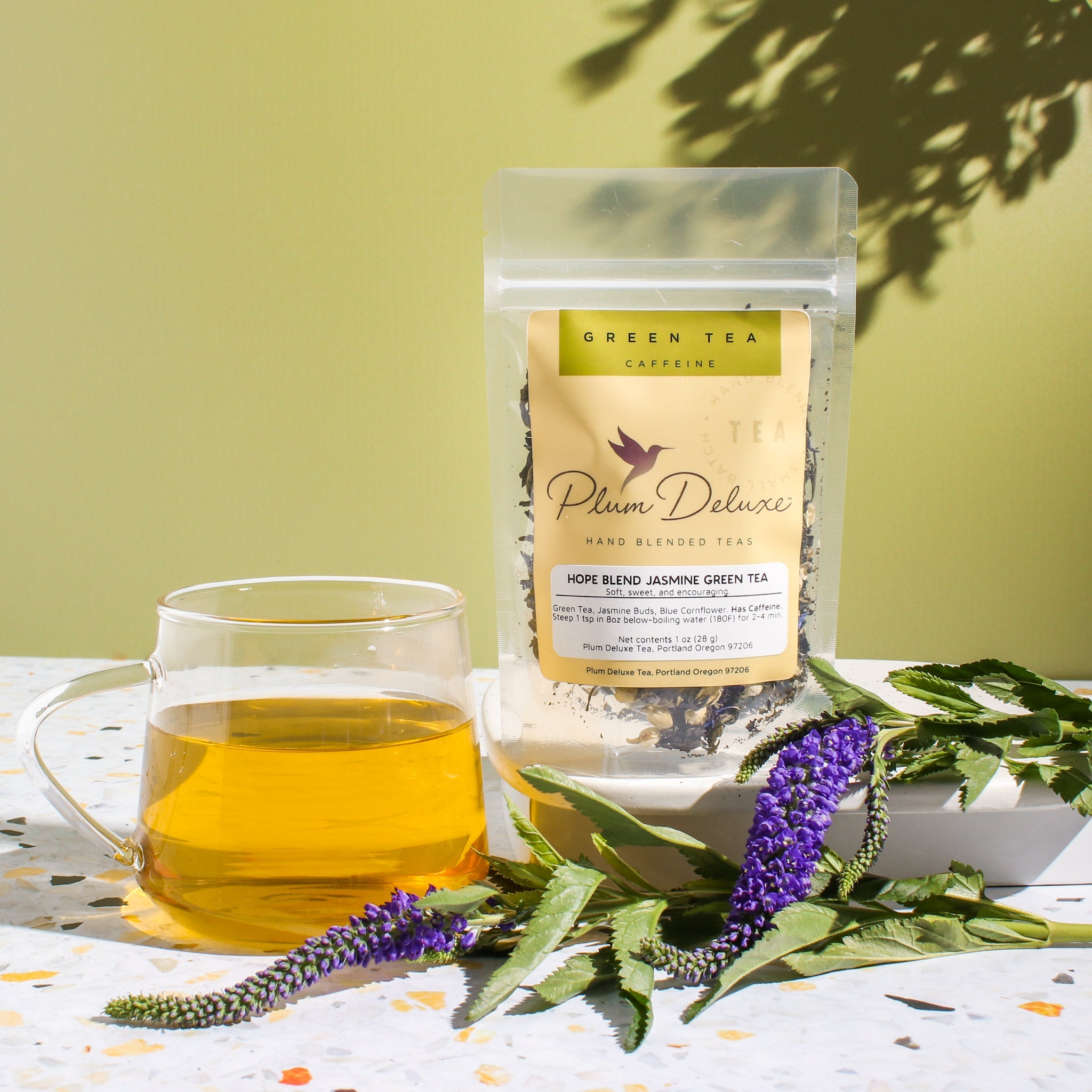 Plum Deluxe Hope Blend Green Tea (Jasmine) in a lifestyle setting, showcasing the product packaging and tea ingredients.
